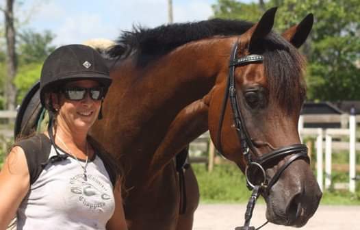 Riding instructor Gillian Muir smiling next to a bay Arabian show horse.