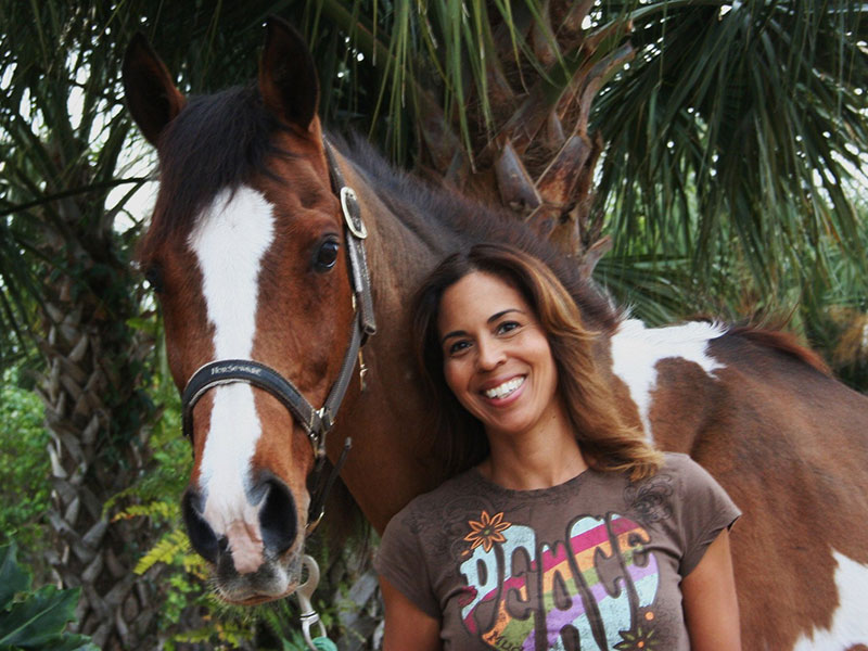 Smiling woman standing next to brown and white paint horse